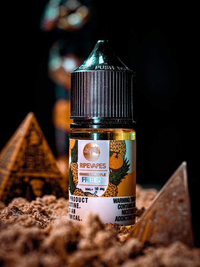 Close-up of an orange pineapple flavored vape liquid bottle amidst decorative pyramids.